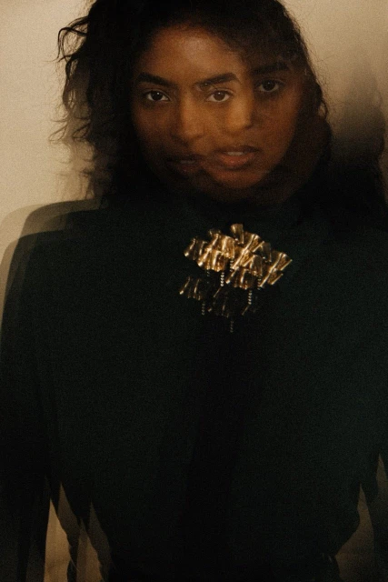 Portrait of an adult woman with dark hair wearing a dark green top with a gold and black brooch, long exposure and motion blur. 