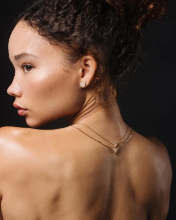 Close-up portrait of a woman wearing diamond triangle earrings and gold chain necklaces against a dark background