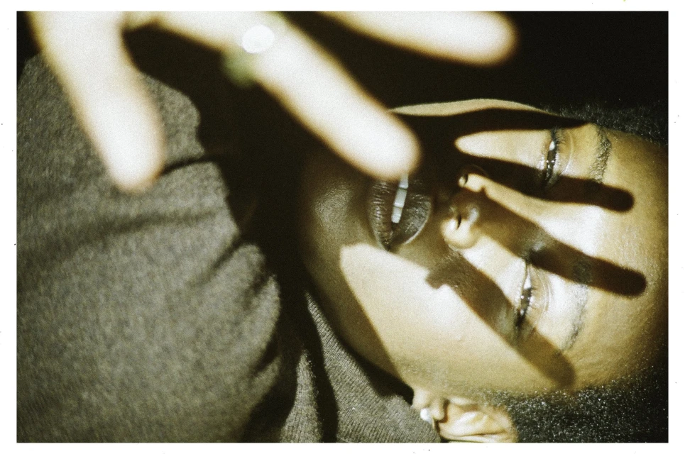 Close-up shot of an adult female with her hand partially covering her face creating shadows in indoor setting with natural lighting.