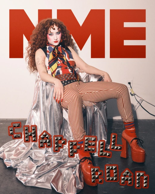 Chappell Roan sits in a silver chair against a white wall with 'NME' text. The photo showcases a mix of retro and modern styles.