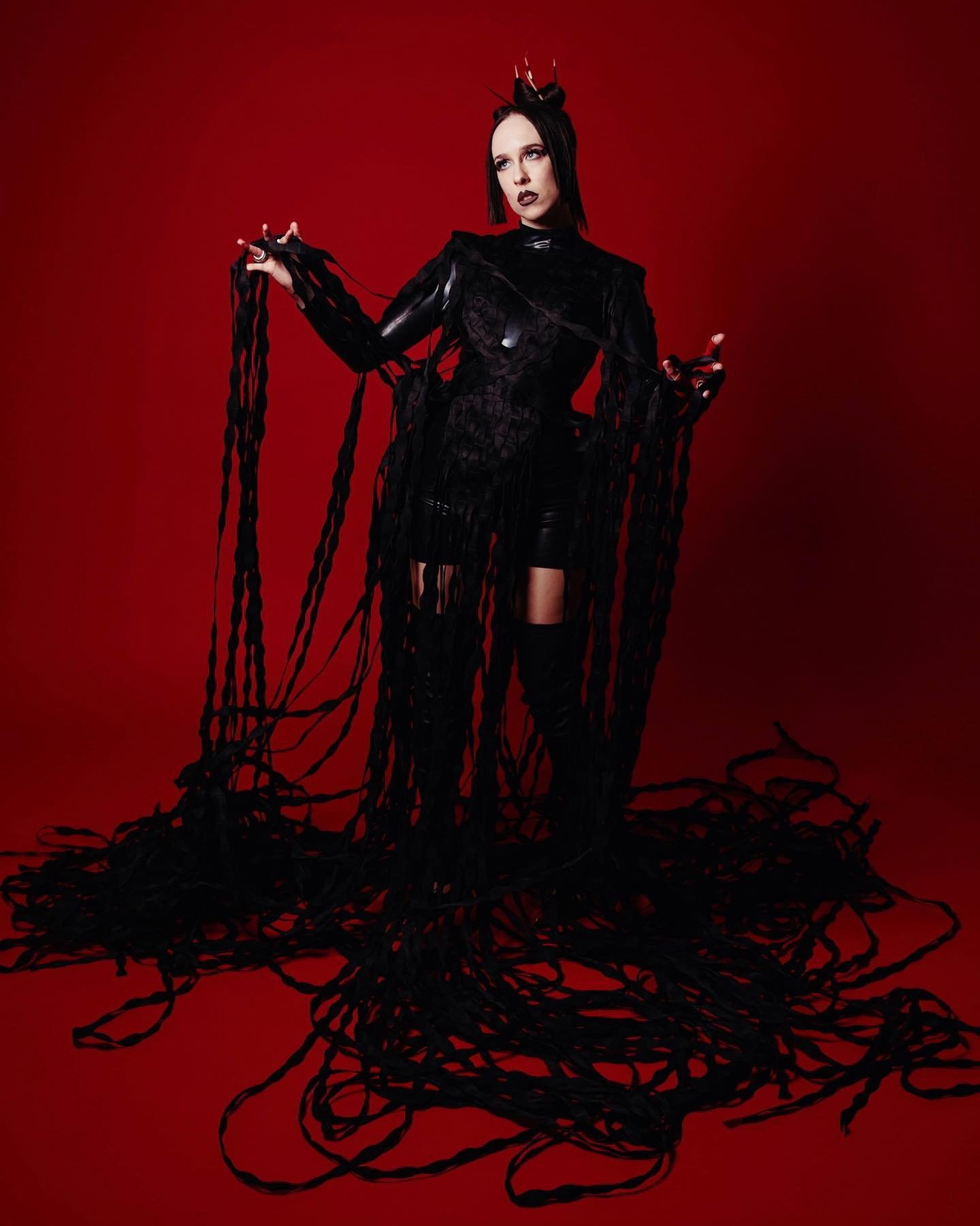 Woman in a black costume with dramatic black strands in a photo studio against a red backdrop, creating a striking and theatrical image.