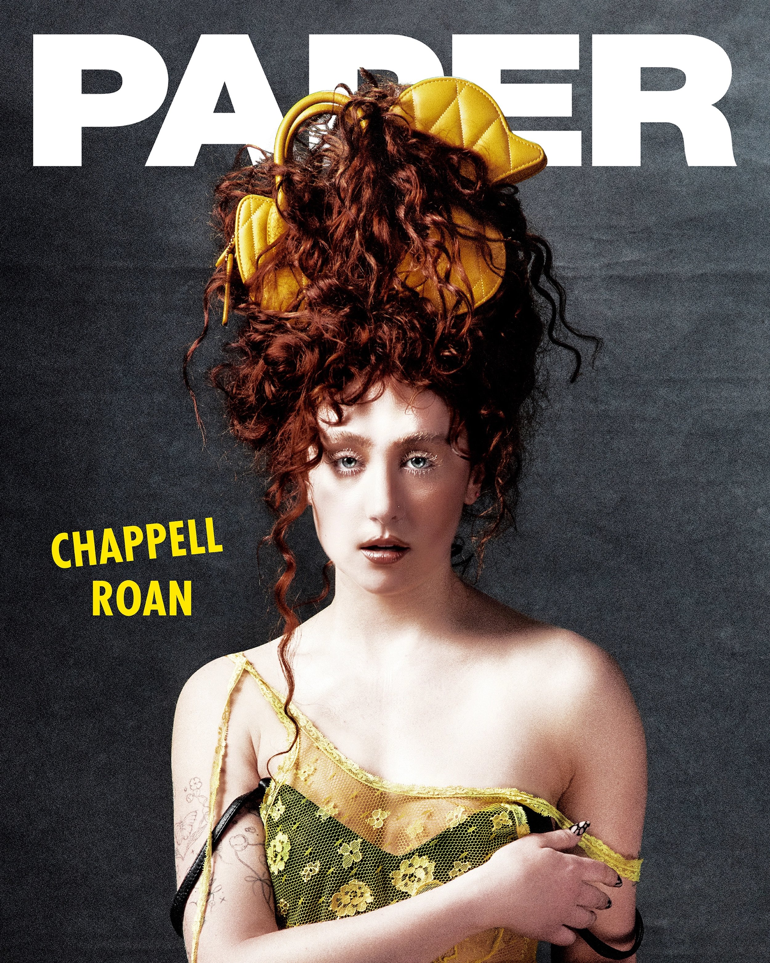Editorial-style shot of Chappell Roan on PAPER Magazine cover with statement red curly hair and yellow hat-like accessory.