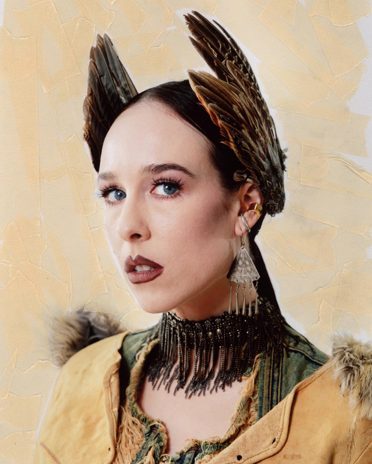 Woman in feathered headpiece and beaded choker, facing viewer. A portrait with neutral background. Earring detail. Shoulder length shot.
