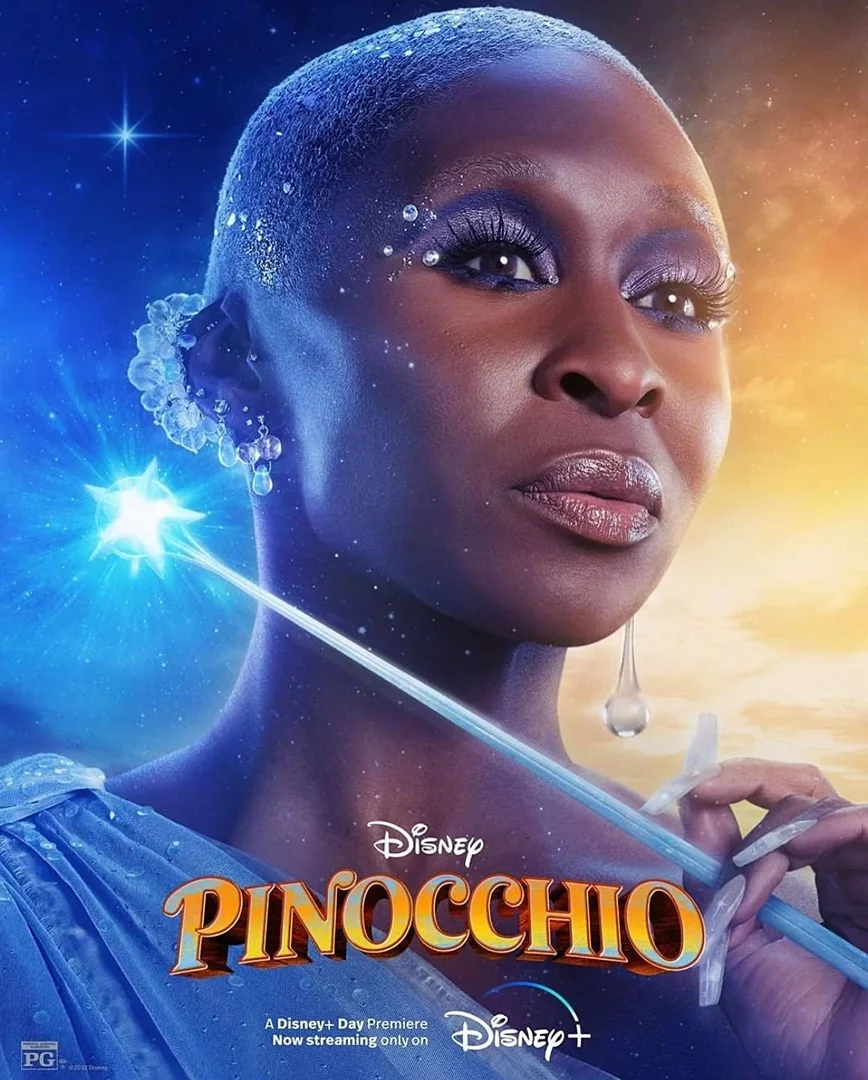 Portrait of Cynthia Erivo as the Blue Fairy from Disney's Pinocchio holding a magic wand with glitter makeup in a blue-lit background.