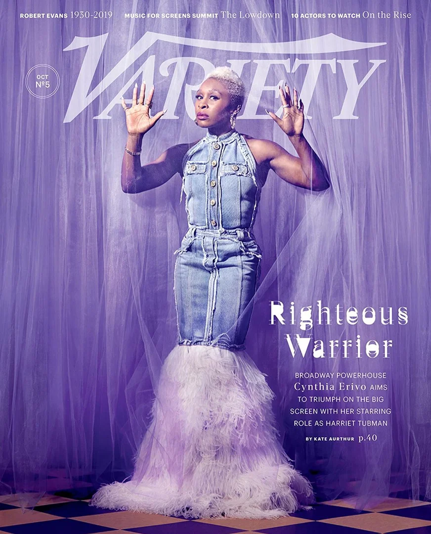 Cynthia Erivo on Variety magazine cover. The woman is in a denim dress with white feathers at the hem, standing in front of a curtain.