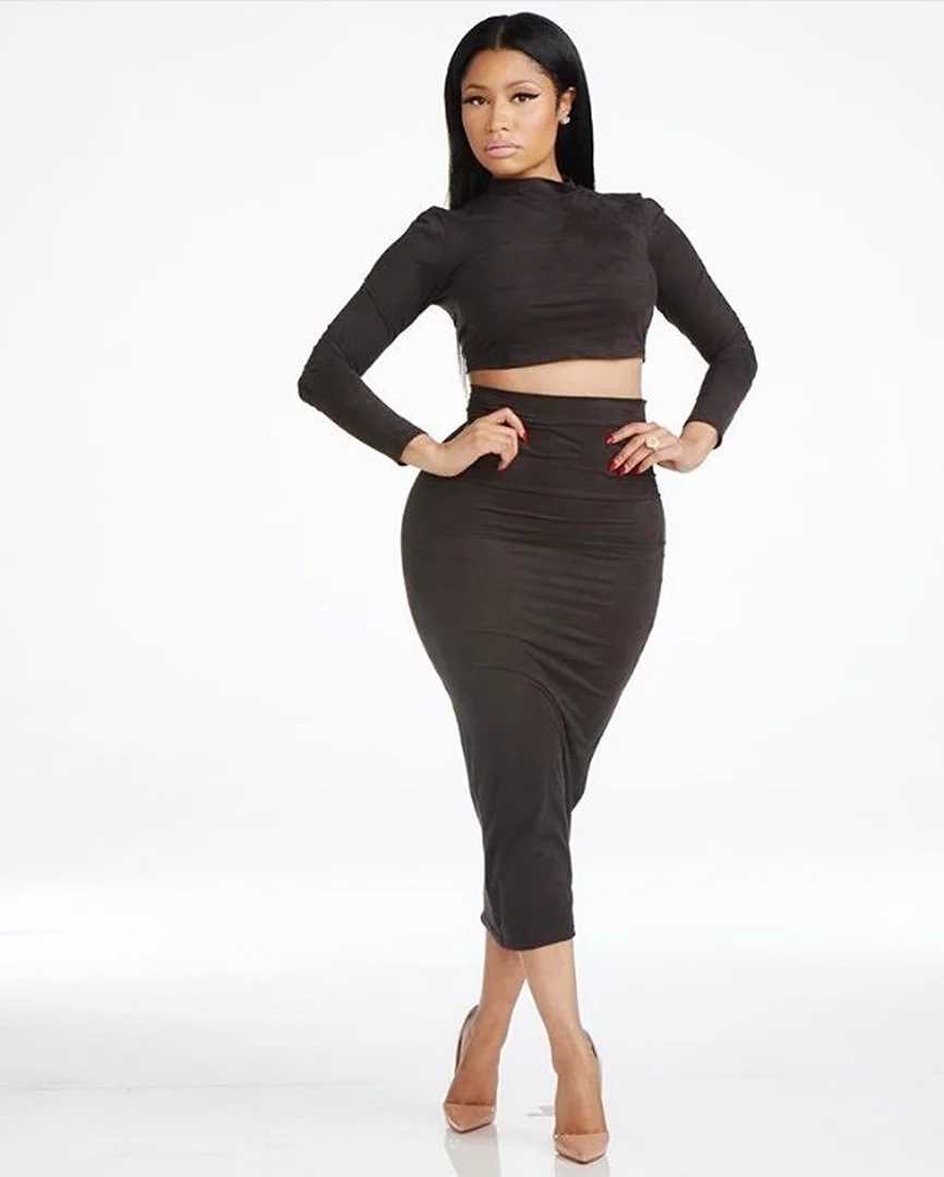 Woman in a two-piece dress with long sleeves and heels posing in a photo studio. Full body shot with solid white background.