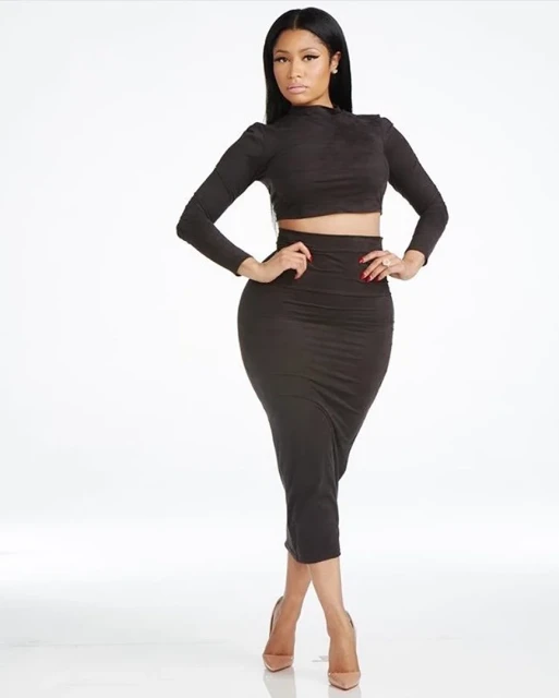 Woman in a two-piece dress with long sleeves and heels posing in a photo studio. Full body shot with solid white background.