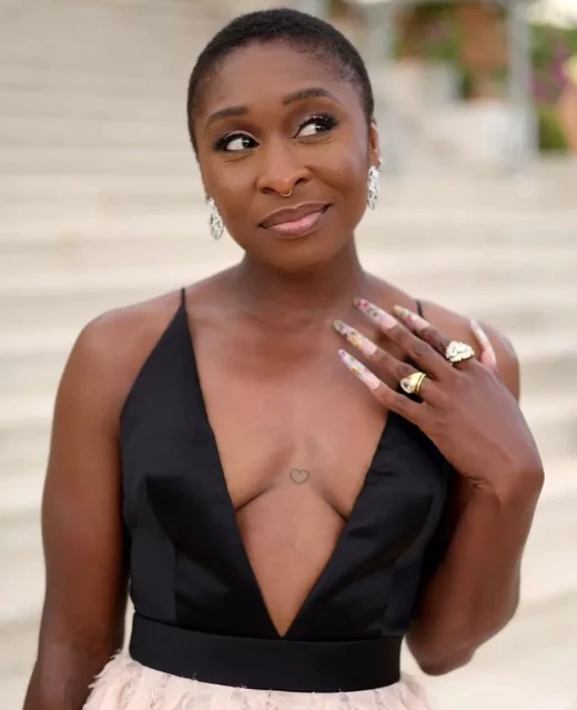 Close-up of a stylish adult woman with short hair wearing a black gown with jewelry, posing in a well-lit outdoor environment.