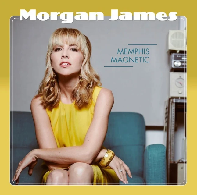 Portrait of Morgan James, blonde female singer-songwriter, wearing a yellow dress sitting on a blue chair with musical equipment in the background.