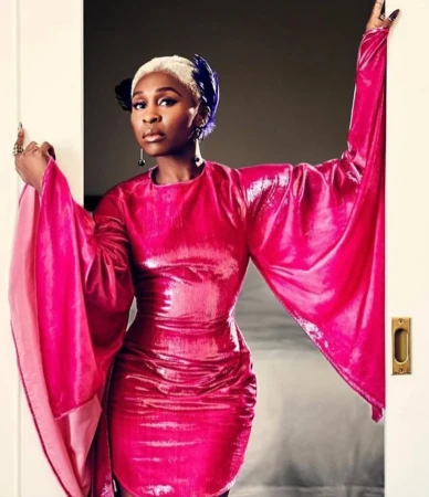 Portrait of Cynthia Erivo wearing a vibrant magenta dress with long dramatic sleeves while posing in a doorway.