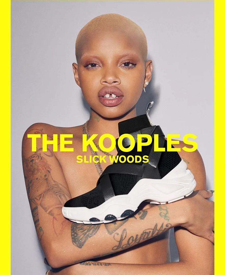Close-up of a bald young woman with tattoos holding a black and white sneaker; text overlay for brand, The Kooples.