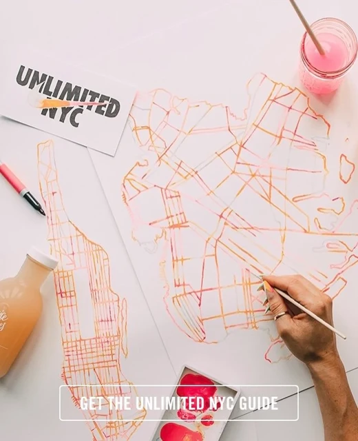 Overhead shot of an artist painting a map of New York City with pink and orange watercolors, using a brush on white paper, with visible paint supplies.