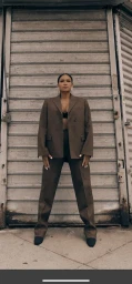 Woman wearing a brown blazer and trousers standing in front of a corrugated metal rolling shutter door.