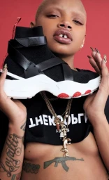 Close-up of a person holding a black sneaker with straps in front of their face against a solid red background