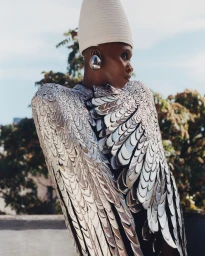 Model wearing a metallic feather cape and tall white hat with a large ear cuff, photographed by Gina Oh in New York