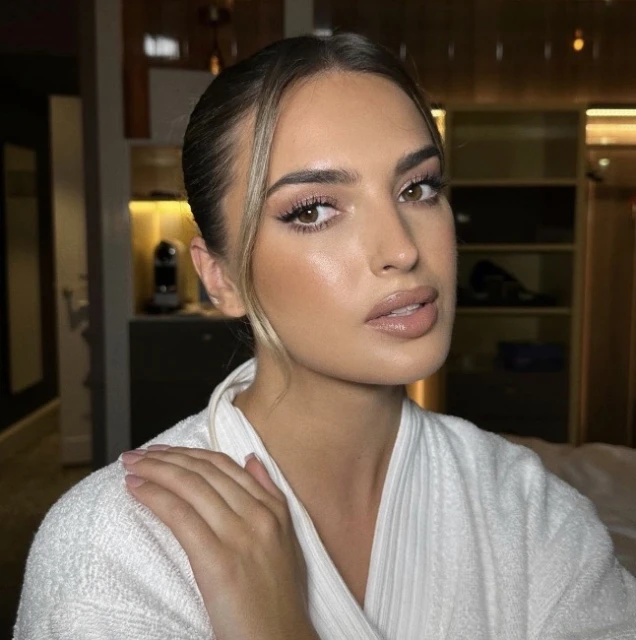 Portrait of a woman with brown hair wearing a white robe in an indoor setting, showcasing soft, natural makeup and elegant styling.