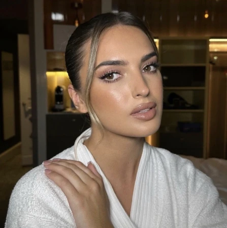 Portrait of a woman with brown hair wearing a white robe in an indoor setting, showcasing soft, natural makeup and elegant styling.