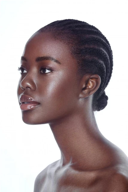 Headshot of a dark-skinned woman with braided hair in profile against a white background. Beauty shot with glossy makeup.