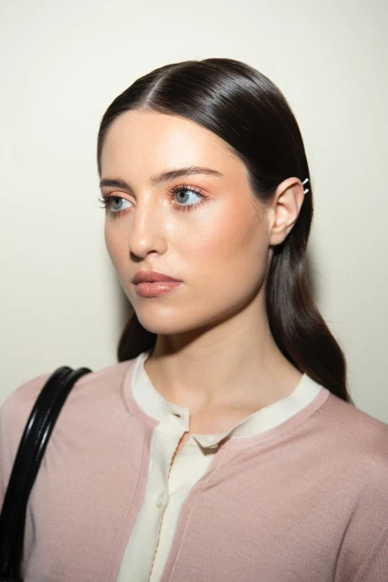 Portrait of a young woman with smooth, dark hair and light eyes wearing a light pink top, posed against a light neutral background.