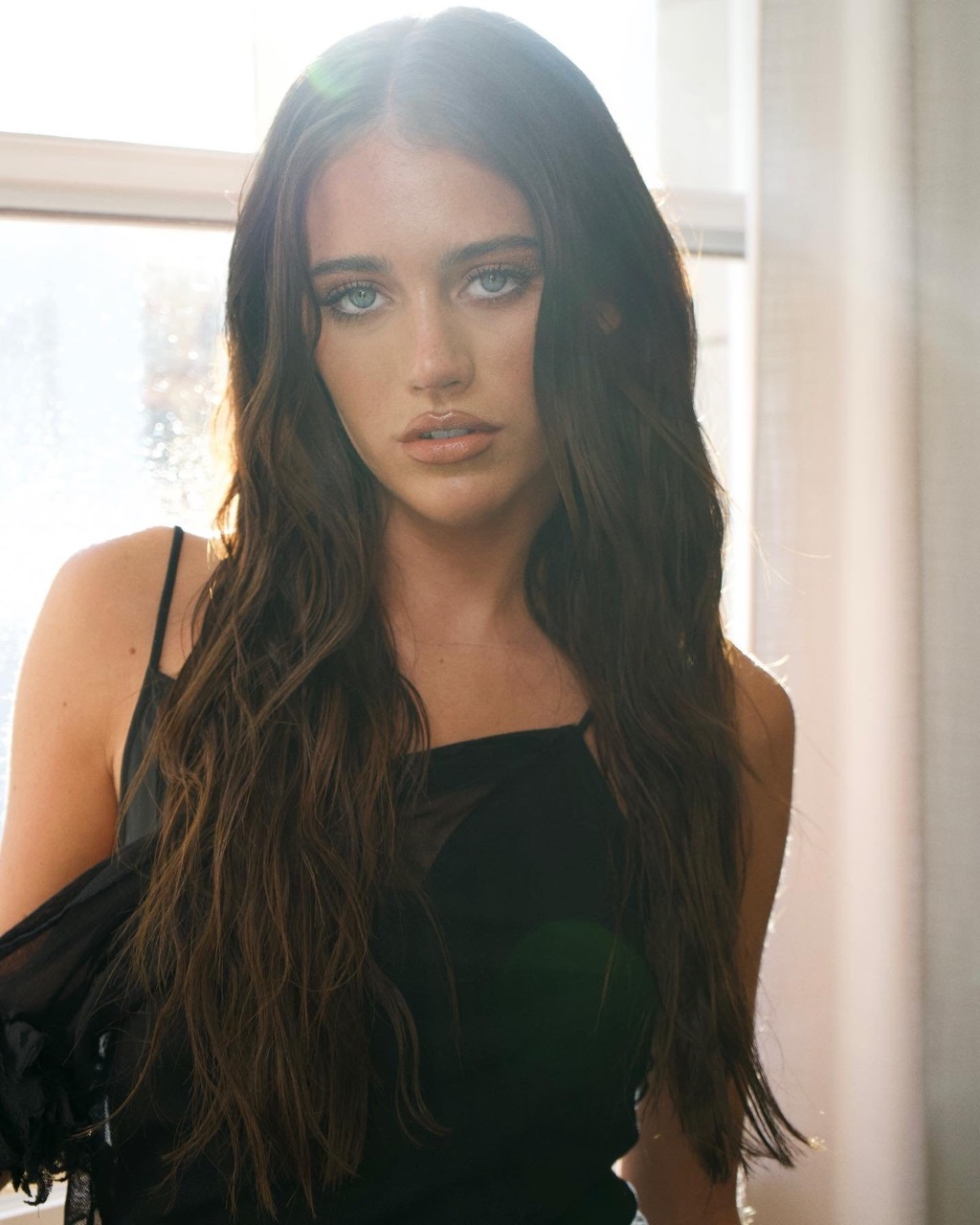 Close-up portrait of a woman with long dark wavy hair wearing a black dress, featuring makeup artistry by Jacinta Spencer.