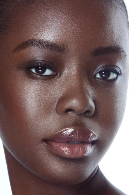 Close-up portrait of a beautiful Black woman with glossy lips and flawless skin against a bright white background in a beauty campaign.