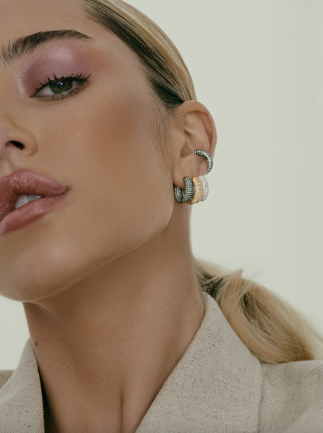 Close-up portrait of a woman wearing textured hoop earrings and a beige jacket against a neutral background