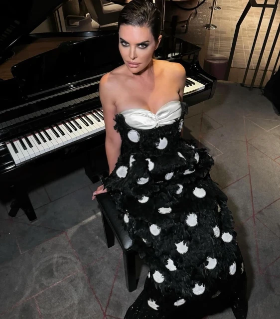 Adult female poses on a piano bench, wearing a strapless black and white polka dot gown in an indoor setting. Formal wear and piano.