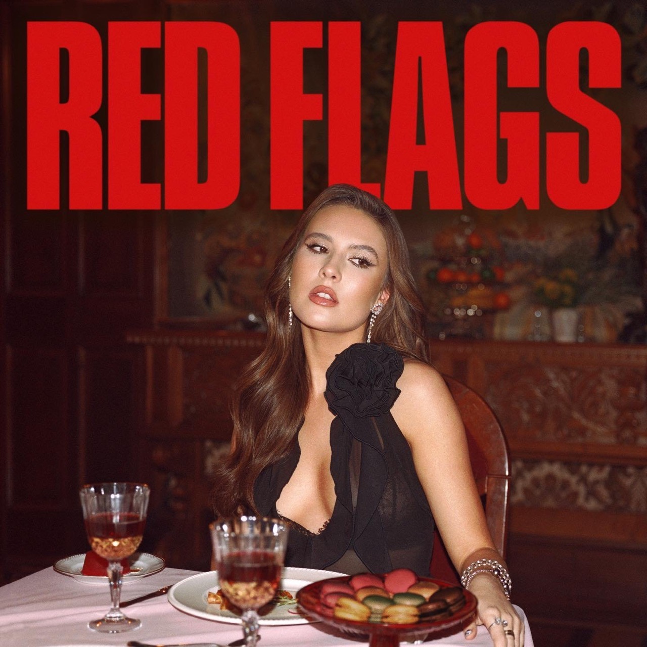 Woman in a black dress sits at a table with wine glasses and macarons, illuminated by warm, soft light. 'RED FLAGS' in red text.