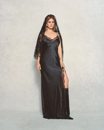Woman in a black satin slip dress and lace veil poses in a studio, showcasing a blend of fashion and fine art aesthetics.