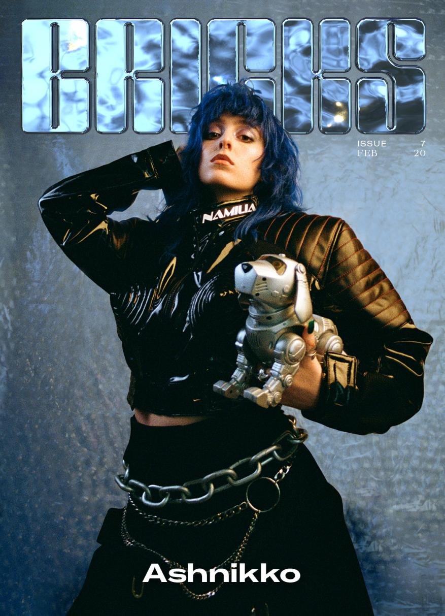 Magazine cover featuring a young woman with blue hair, wearing a black jacket and skirt, holding a silver toy robot dog.
