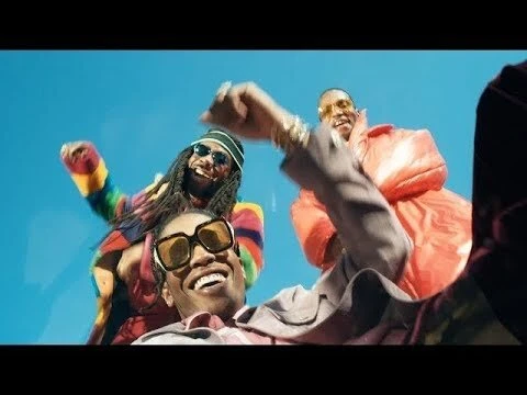 Three men in colorful streetwear and sunglasses smiling outdoors against a bright blue sky.