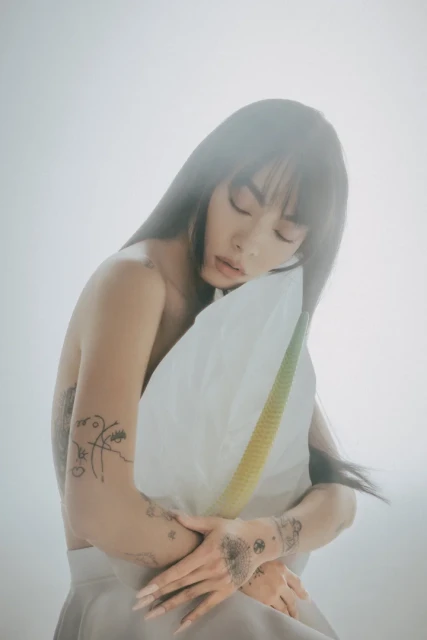 Portrait of a woman with long dark hair, holding a white anthurium flower with a yellow spadix in a soft, misty light.