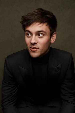 Portrait of a young adult man with short brown hair, wearing a black turtleneck and suit jacket, looking left against a neutral backdrop.