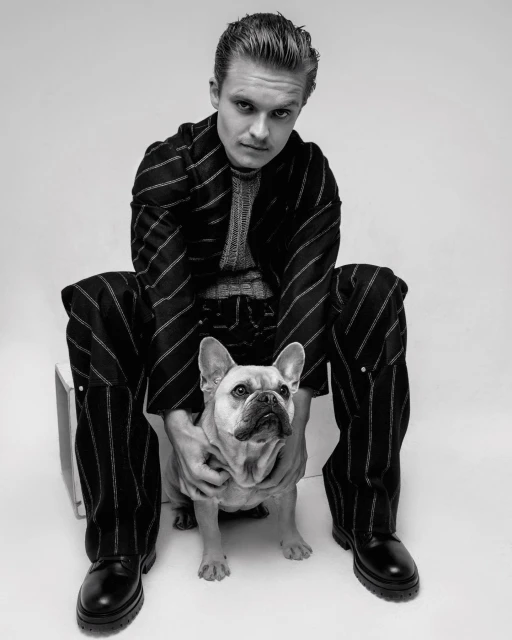 Portrait of an adult male in a striped suit sitting with a French bulldog, captured in a black and white photo studio setting.
