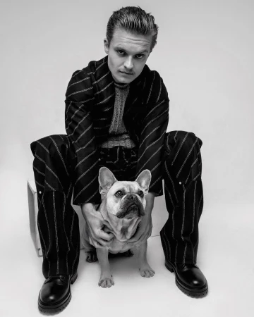 Portrait of an adult male in a striped suit sitting with a French bulldog, captured in a black and white photo studio setting.