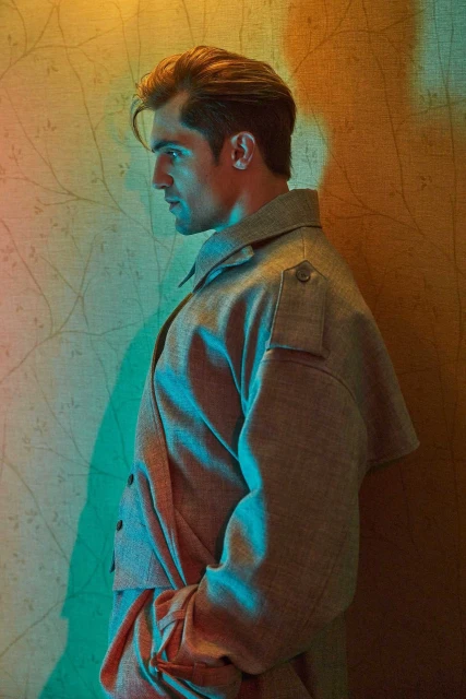 Stylish man in tweed suit posing against a textured wall with artistic lighting. Fashion, portrait, and studio shot.