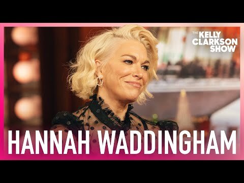 Close-up studio shot of Hannah Waddingham, with blond wavy hair, wearing a black polka dot top, in front of a blurred background.