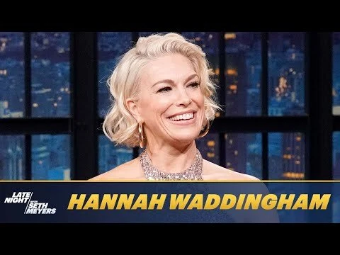 Close-up of Hannah Waddingham in a television studio setting with a city skyline backdrop, wearing a sequin top and gold earrings.