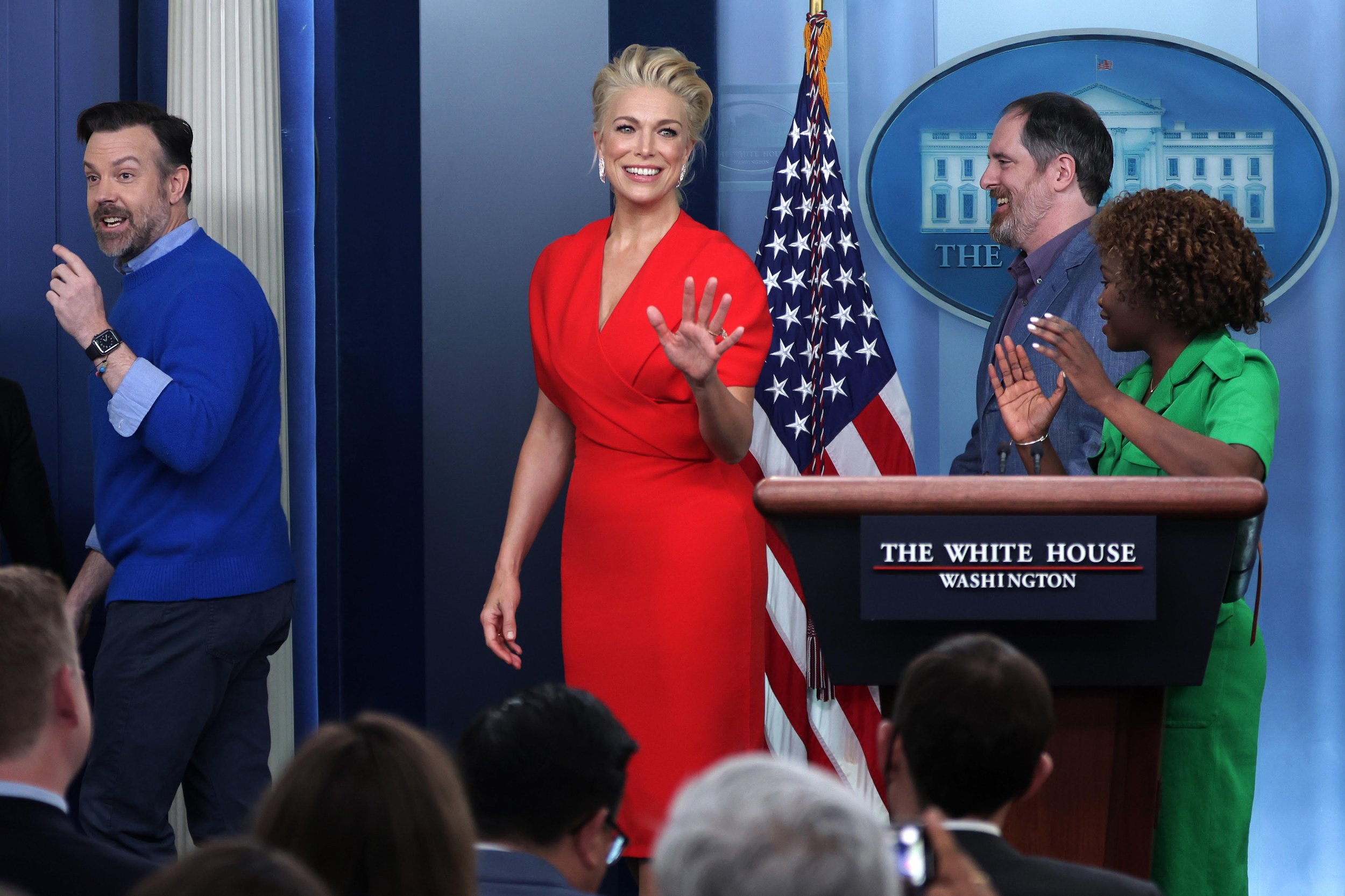 Hannah Waddingham waves in a vibrant red dress alongside Jason Sudeikis at a White House event, with a crowd in the foreground.