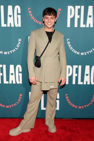 Tom Daley standing on a red carpet wearing a sage green suit and black t-shirt against a branded teal backdrop styled by James Yardley