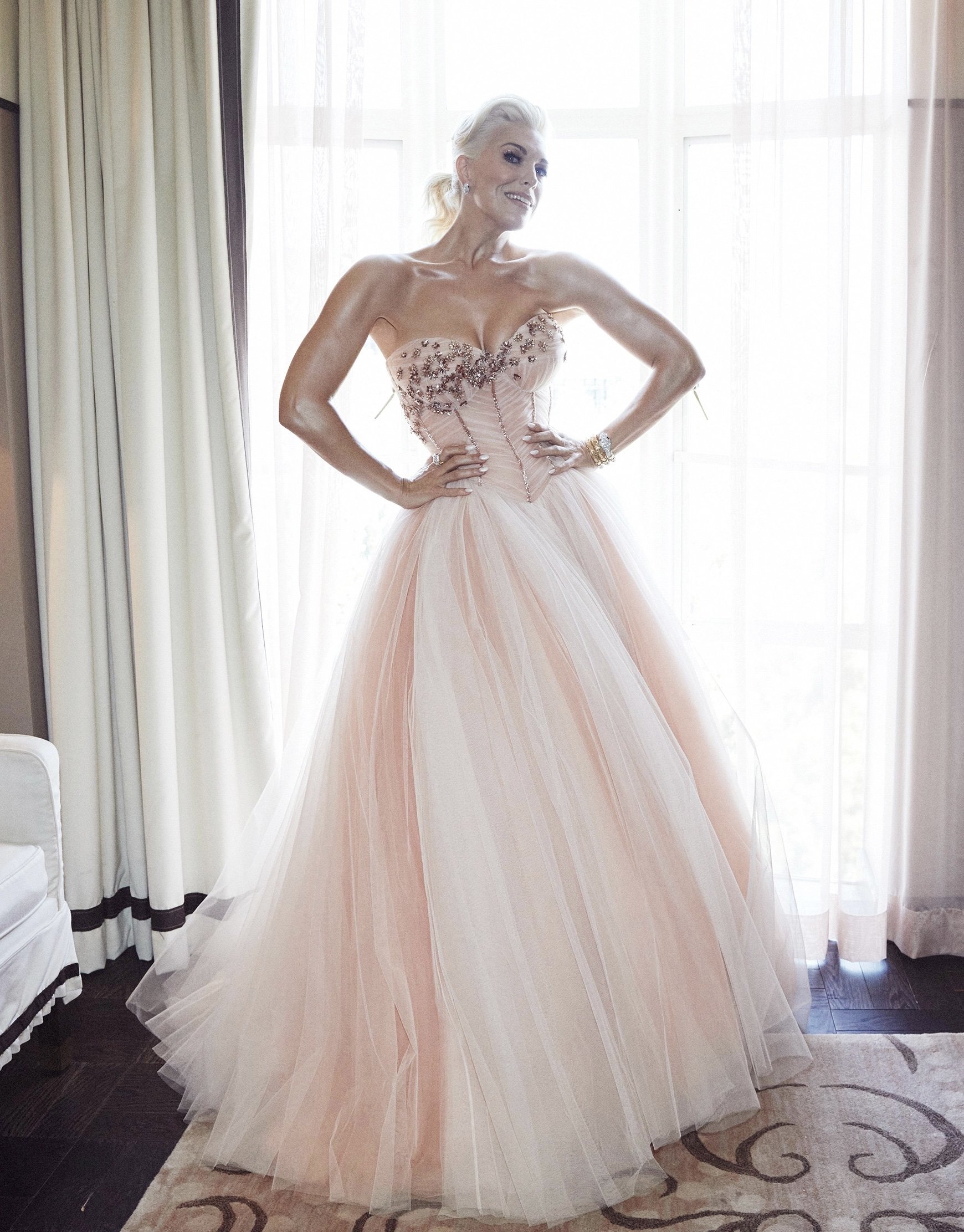 Elegant woman in a strapless formal gown with an embellished bodice and a flowing tulle skirt poses against window light.
