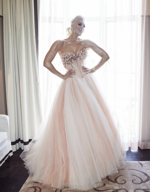 Elegant woman in a strapless formal gown with an embellished bodice and a flowing tulle skirt poses against window light.