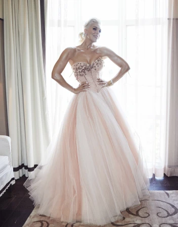 Elegant woman in a strapless formal gown with an embellished bodice and a flowing tulle skirt poses against window light.