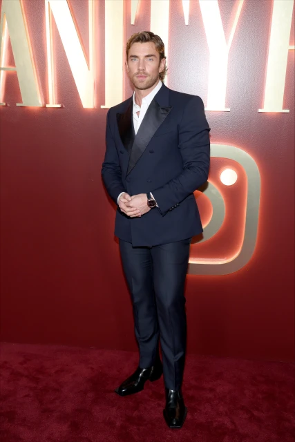Actor Chris Brochu poses in a navy suit at a red-carpet event with a Vanity Fair logo in the background; he's wearing a white dress shirt.