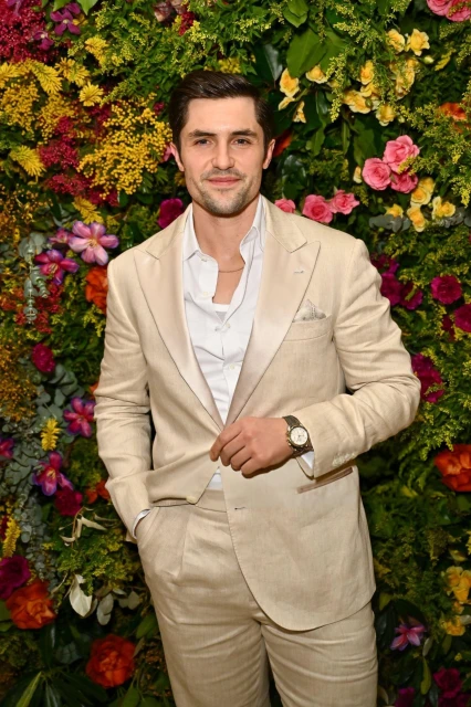 Portrait of a handsome adult male wearing a beige suit and posing in front of a flower wall. Formal wear fashion and celebrity style.