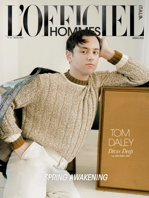 Magazine cover featuring Tom Daley in a beige knit sweater and white pants, leaning on a tan frame with the title 'L'Officiel Hommes'.