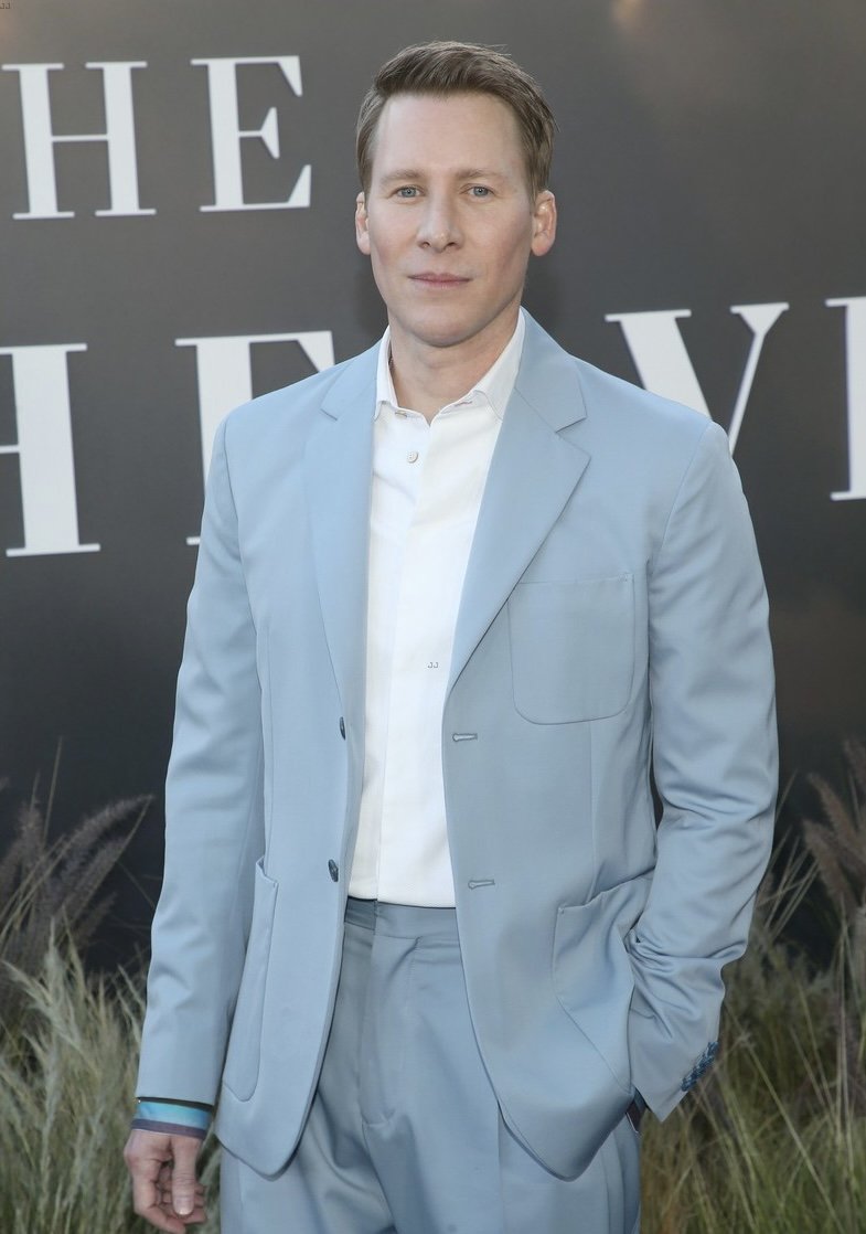 Man in a light blue suit and white shirt standing against a dark wall with white lettering in London