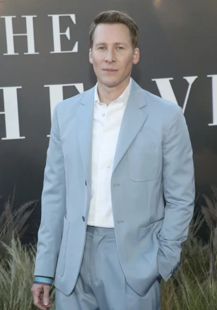 Man in a light blue suit and white shirt standing against a dark wall with white lettering in London