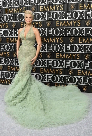 Woman in elegant gown at the Emmy Awards on a branded step-and-repeat backdrop, celebrating entertainment and fashion in a formal setting.