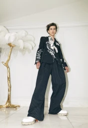 Model wearing dark pinstripe suit with white graphic pattern and chunky white shoes in a styled interior